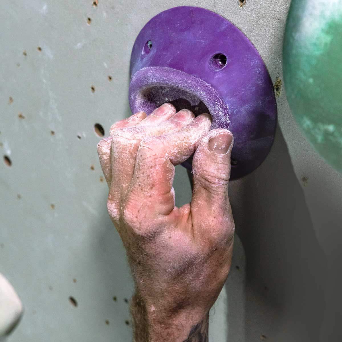 A climbers hand covered with liquid chalk, gripping a rock climbing hold.